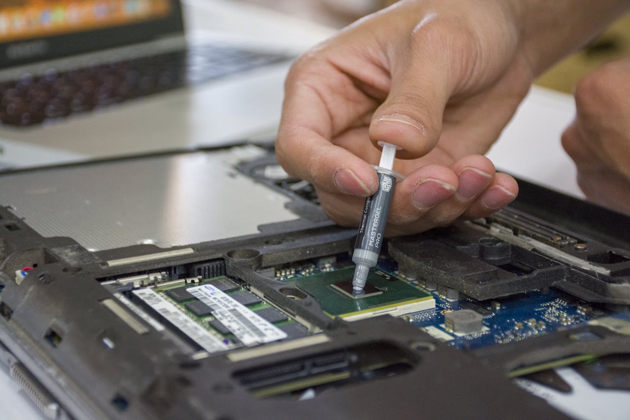 Inicio Close-up of hand applying thermal paste to a laptop microchip for maintenance.